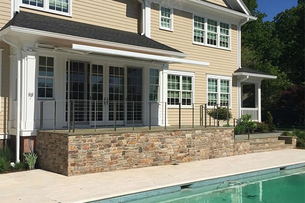 Cream retractable awning deployed above a stone-edged pool on a beige house