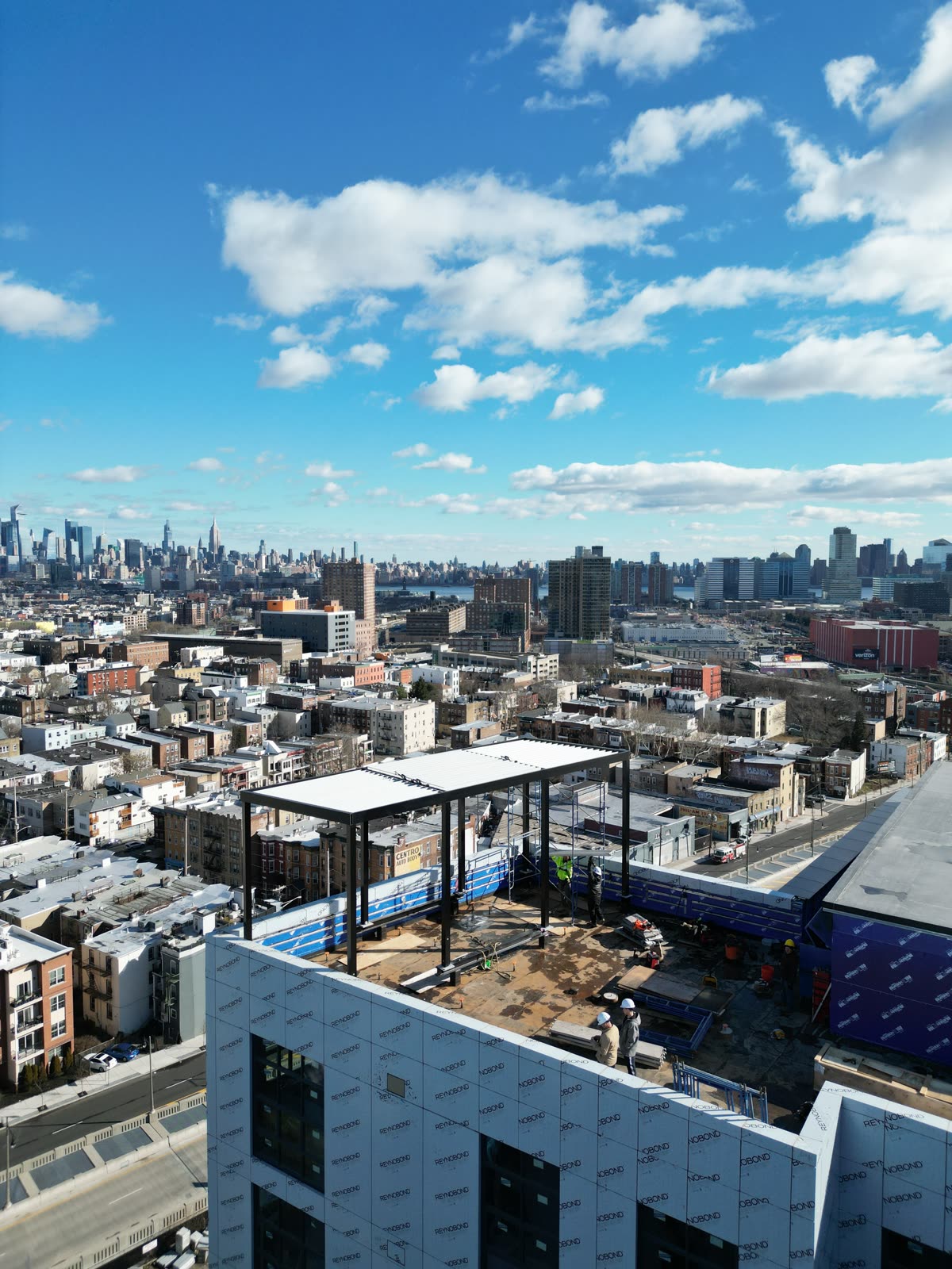 Drone view of a rooftop steel pergola frame being erected with the Manhattan skyline in the distance
