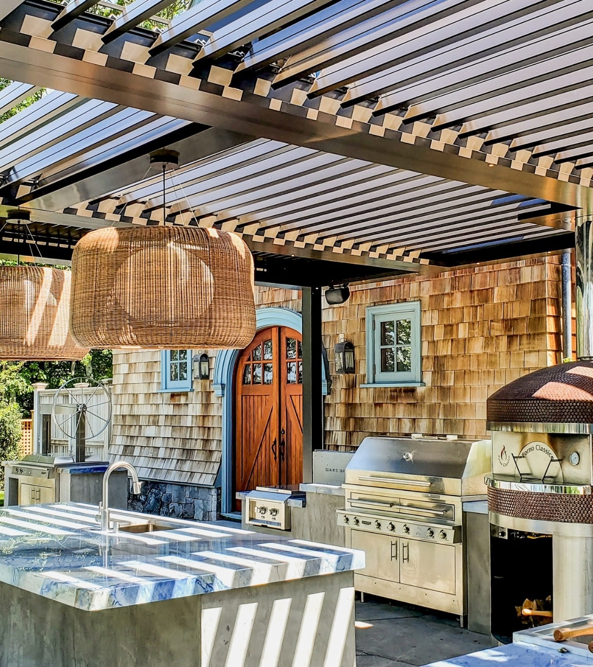 Outdoor kitchen with pizza oven, gas grill, and marble island under a slatted pergola