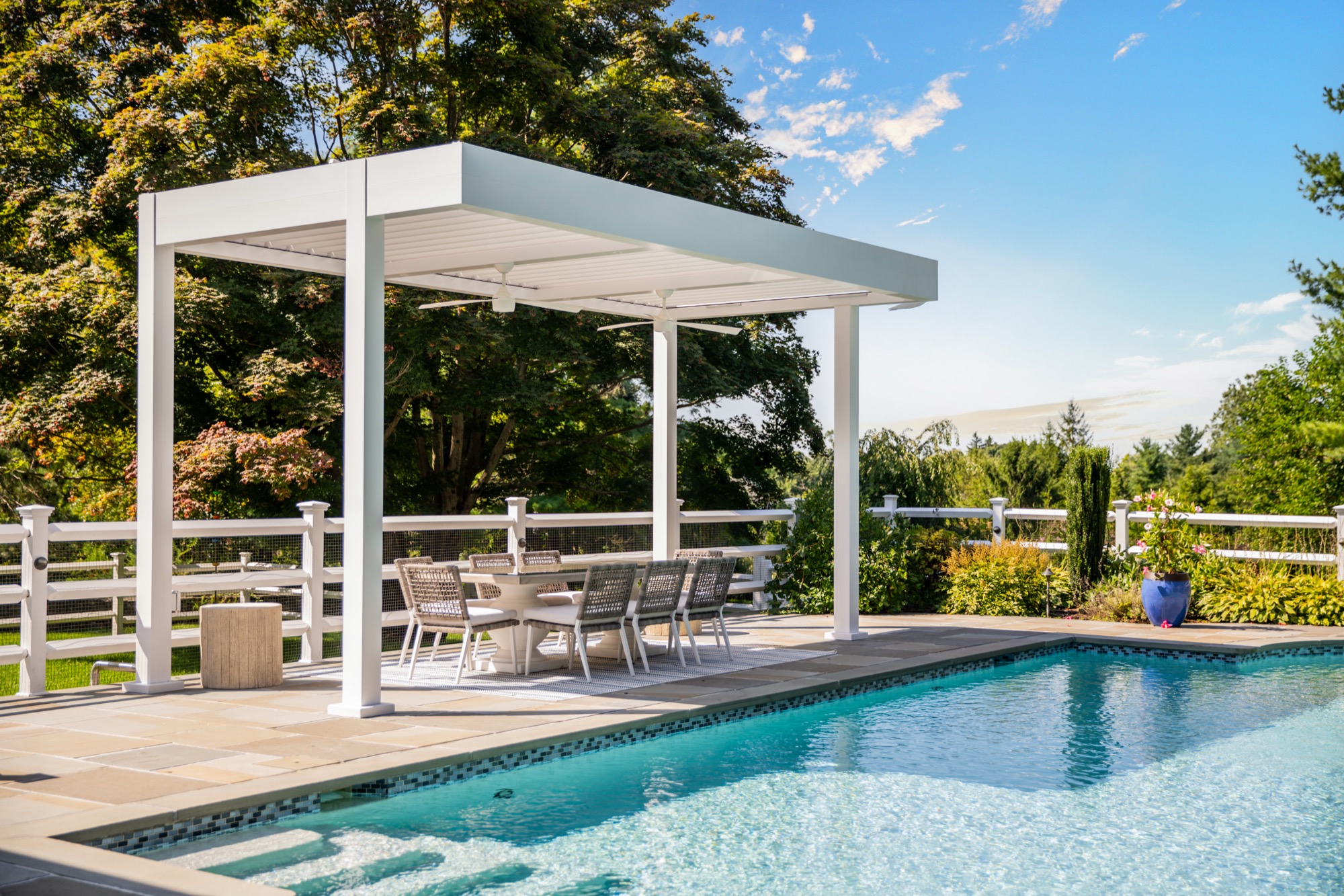 White three-bay Azenco R-Blade louvered roof seen from the Montvale backyard — three equal bays attached to the home and carried on columns matched to the front of the house, over an open patio