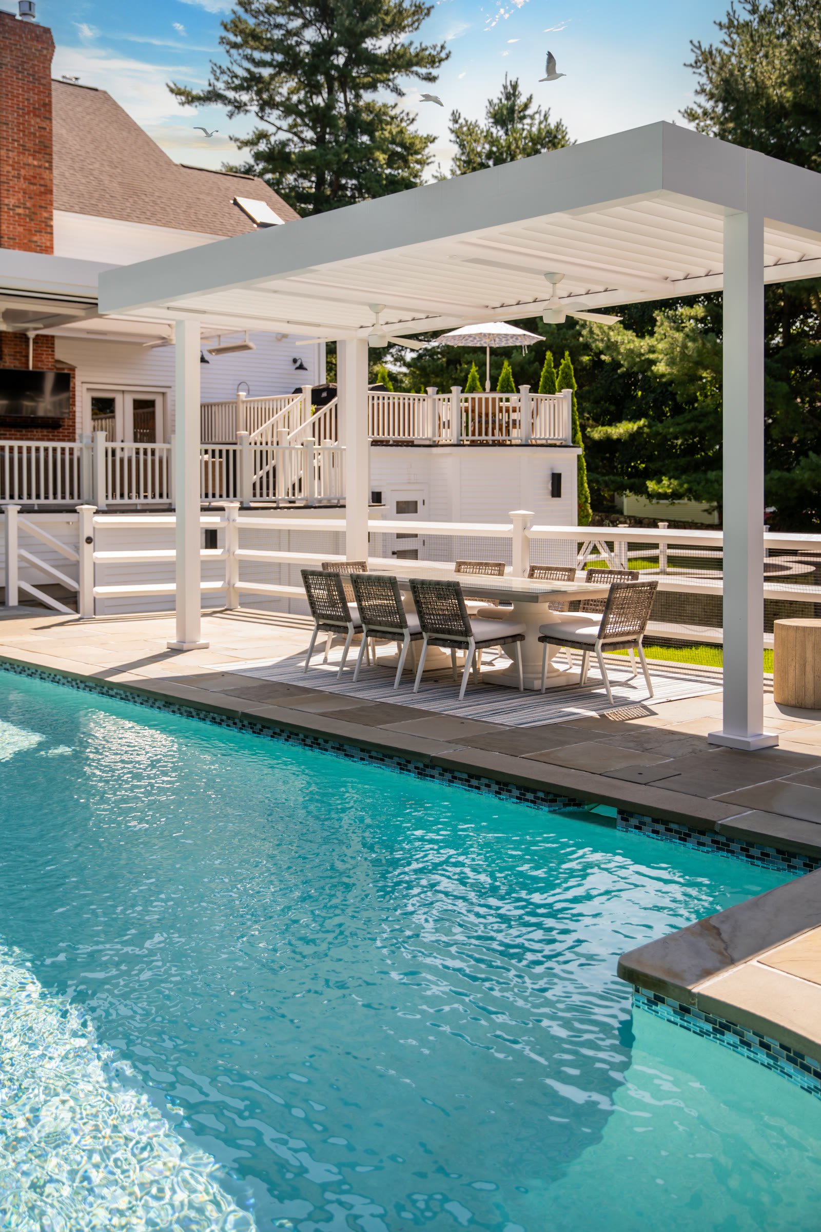 Freestanding white aluminum louvered pergola beside a pool